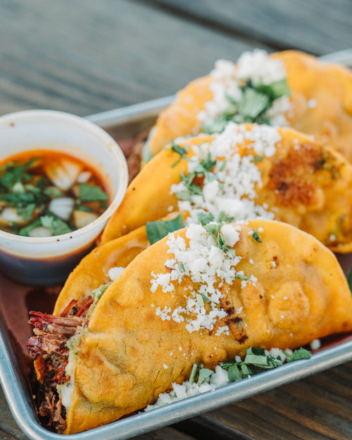 Birria tacos on a tray with a cup of consommé