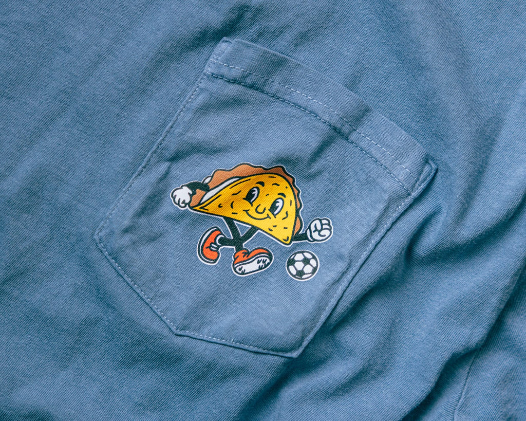 Soccer Taco Tee in faded blue, close-up of the chest-pocket taco mascot